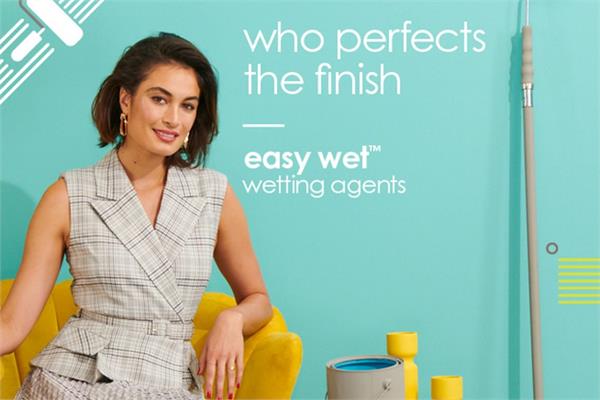 A woman in front of a blue wall painted with coatings containing the Easy-Wet wetting agents of Ashland