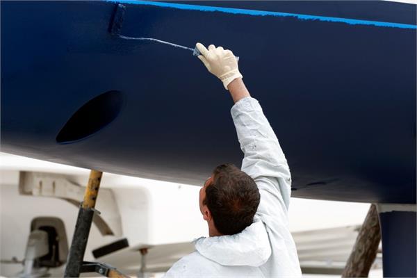 An operator in a white suite coating a blue marine hull