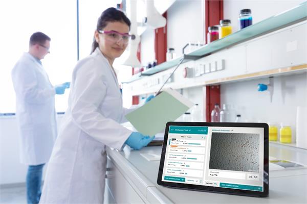 A woman in a lab coat looks towards the screen of a tablet with the COATINO Defect Detention software of Evonik